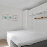 Schlafzimmer mit weißem Bett, weißen Schränken und drei Bildern an der Wand.