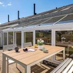 Terrasse mit Tisch und Stühlen vor einer Glasveranda mit Blick auf den Garten.