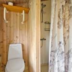 Badezimmer mit Dusche, Toilette und Holzwandverkleidung.