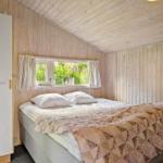 Schlafzimmer mit Bett, Holzwand und Fenster mit Blick auf Grün.