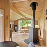 Wohnraum mit Holzwand, Kaminofen und Sitzgelegenheiten. Durchgang zu weiterem Raum mit Fenster.