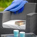 Gartenstuhl mit Kissen, Decke und Buch. Auf Tisch stehen zwei Tassen.