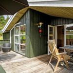 Terrasse mit Holzboden, Stuhl, Tisch und Sonnenschirm vor einem Haus mit grünem Holzverkleidung.