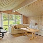 Wohnzimmer mit Holzwand, Sofa, Esstisch und Sessel vor großem Fenster.