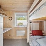 Schlafzimmer mit Hochbett, Fenster und weißen Schränken an Holzwand.