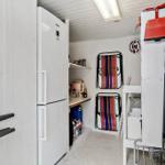 Küche mit Kühlschrank, Arbeitsfläche und aufgehängten Reinigungswerkzeugen.