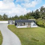 Ein modernes Haus mit dunklem Dach und weißer Umrandung, umgeben von Grünfläche und Bäumen.