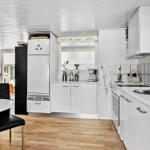 Küche mit weißen Schränken, Holzboden und Küchenzeile mit Spüle und Kochfeld.