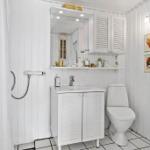 Badezimmer mit Dusche, Waschbecken und Toilette. Weiße Holzwandverkleidung und Fliesenboden.