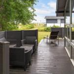 Deck with seating area and view of grassland and adjacent building.
