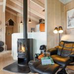 A room with wooden walls, wood stove, and black leather recliner. Wall clock and picture on the wall.
