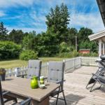 Terrasse mit Tisch, Stühlen und Grill. Grünflächen und Bäume im Hintergrund.