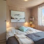 Schlafzimmer mit Bett, Wandbild und Bücherregal. Holzwand und Fenster mit Blick nach draußen.