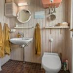 Badezimmer mit Holzwand, Waschbecken, Toilette und Handtuchhaltern.