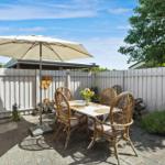 Terrasse mit Tisch, Stühlen und Sonnenschirm. Hinterhof mit Holzzaun und Pflanzen.