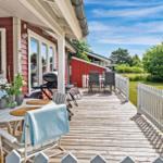 Terrasse mit Tisch, Stühlen und Grill. Roter Holzaufbau, weißer Zaun und Garten.