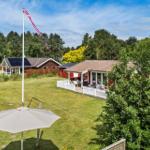 Roter Holzhaus mit weißem Zaun und Garten unter blauem Himmel.