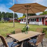 Terrasse mit Tisch, Stühlen und Sonnenschirm. Roter Holzaufbau im Hintergrund.