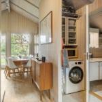 Küche mit Waschmaschine, Essbereich mit Tisch und Stühlen, Holzwände und Fenster zum Garten.