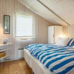 Schlafzimmer mit Holzwand, Bett mit blau-weißem Bettzeug und kleinem Schrank.