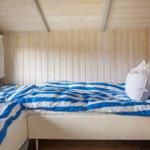 Schlafzimmer mit Holzwand, Bett mit blau-weißem Bettzeug und Fenster mit Vorhang.