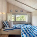 Schlafzimmer mit zwei Betten, Holzwand und Fenster mit Blick auf Grün.