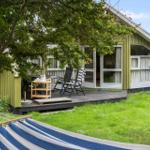 Grünes Ferienhaus mit Terrasse, Garten und Hängematten im Vordergrund.