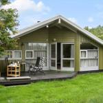 Grünes Holzhaus mit Terrasse, Garten und Fenstern mit Vorhängen.