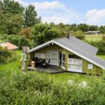 Ein grünes Ferienhaus mit Terrasse und Garten. Umgeben von Bäumen und Gras.