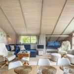 Wohnraum mit Holzdecke, Sofa, Sessel und Essbereich. Fenster mit Blick auf Grün.