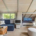 Wohnraum mit Sofa, Schlafcouch, Sessel und TV. Holzdecke und Fenster mit Blick auf Bäume.