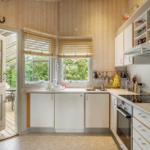 Küche mit Holzwänden, Fenstern und Tür zum Garten. Weiße Schränke und Küchengeräte.