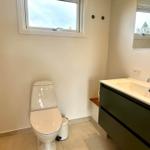 Badezimmer mit Toilette, Waschbecken und Fenster. Spiegel und Holzbank sind vorhanden.