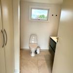 Toilettenraum mit Fenster, WC, Mülleimer und Waschtisch.