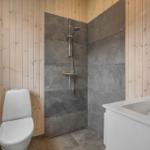 Bathroom with shower, toilet, and sink. Wooden walls and gray tiles.