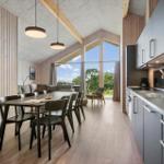 Modern kitchen and dining area with wooden wall and large window view.