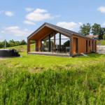 Modern wooden cabin with large glass area and outdoor space with lounge chairs.