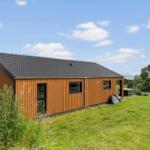 Modern wooden cabin with dark roof on green lawn under blue sky.
