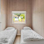 Two beds in a room with wooden walls and window view of outside area.