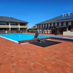 Pool mit Rutsche und Treppe auf rotem Pflaster. Hintergrund: Gebäude mit Solarzellen.