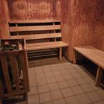 Sauna mit Holzwand, Bänken und Fliesenboden. Heizung im Hintergrund.