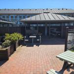 Terrasse mit Pavillon, Tischen und Bechern. Hintergrund: Mehrfamilienhaus.