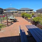 Terrasse mit Picknicktischen, Pflanzen und Wohnhäusern im Hintergrund.
