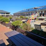 Terrasse mit Picknicktisch, Spielplatz und Gartenbereich vor Wohnhäusern mit Solaranlagen.