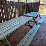 Zwei Holzpicknicktische auf gepflastertem Hof mit hölzerner Umzäunung.