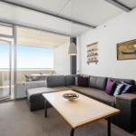Wohnzimmer mit Sofa, Tisch und Balkonblick aufs Meer