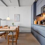 Essbereich mit Tisch, Stühlen und Küchenzeile. Hintergrund: Wohnbereich mit Sofa.