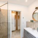 Badezimmer mit Dusche, Waschbecken und runden Spiegel. Holz-Ruder an der Wand.