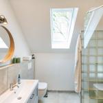 Badezimmer mit Dusche, Waschbecken und Dachfenster. Holzrahmen Spiegel und Glasfliesen.