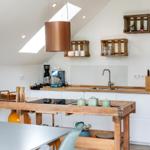 Küche mit Holztisch, weißen Schränken und Dachschrägen. An der Wand hängen Holzkisten.